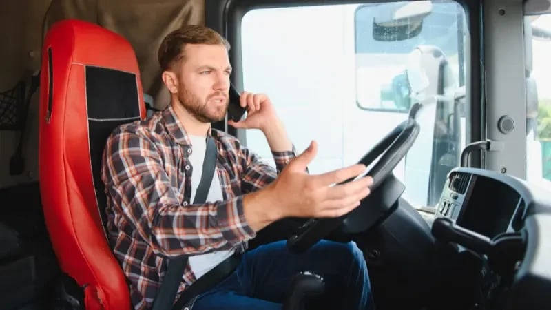 Male truck driver talking on smartphone while sitting in cab of truck