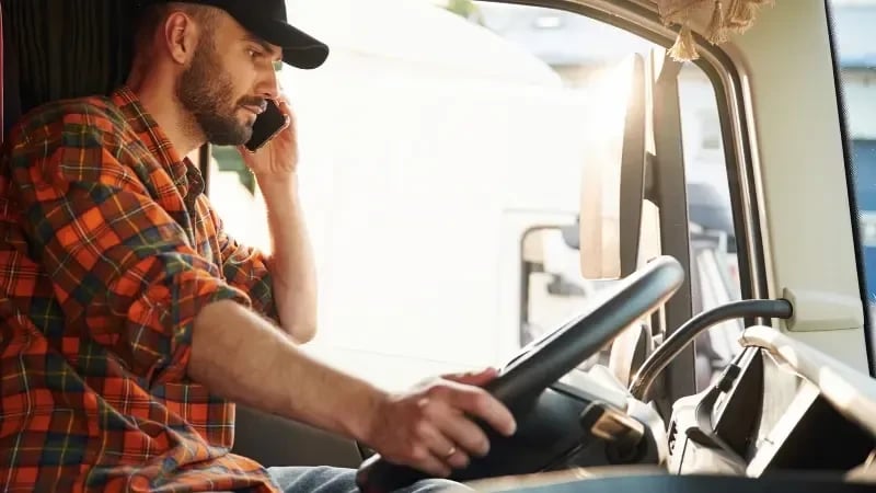 A male truck driver with a mobile phone to his ear, while sitting in the truck cab