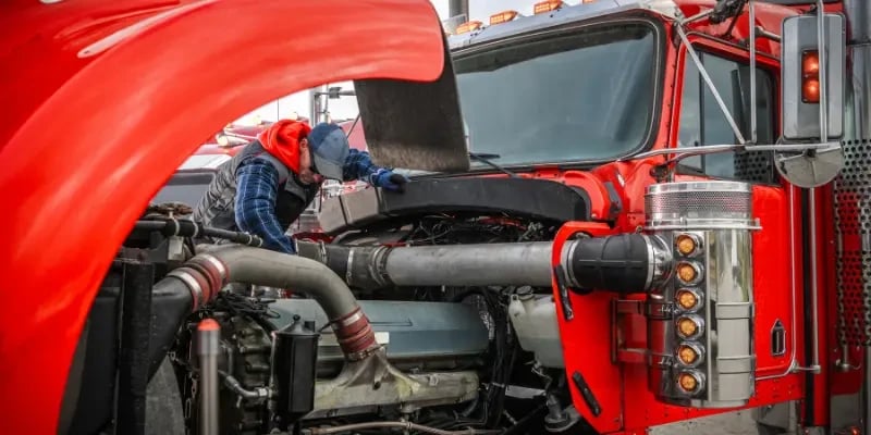 Mechanic inspecting the engine of a red semi-truck with the hood open